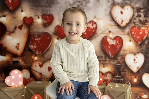 Little 3 year old sitting on a white stool on a valentines set up with hearts. He is here for Kanas City V day mini sessions with Susy photo LLC